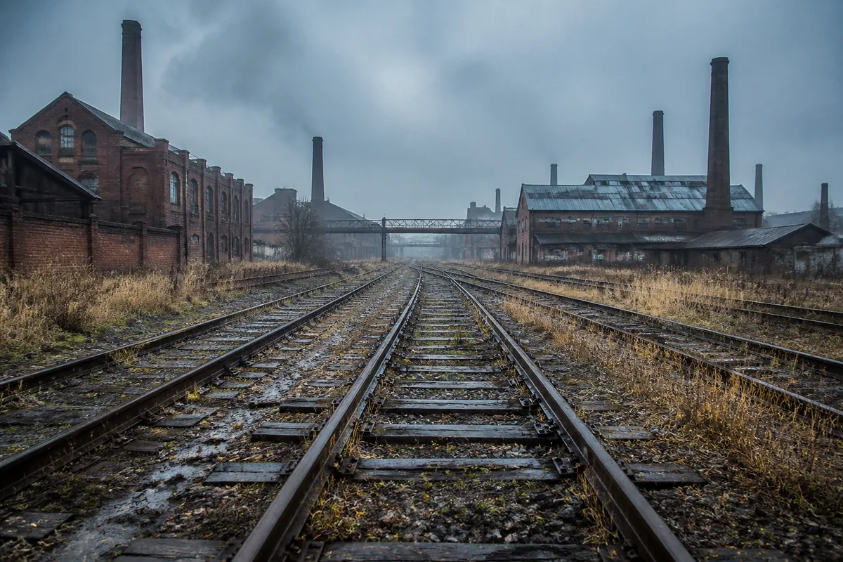 Rails de chemin de fer et bâtiments industriels du XIXe siècle sous un ciel bas