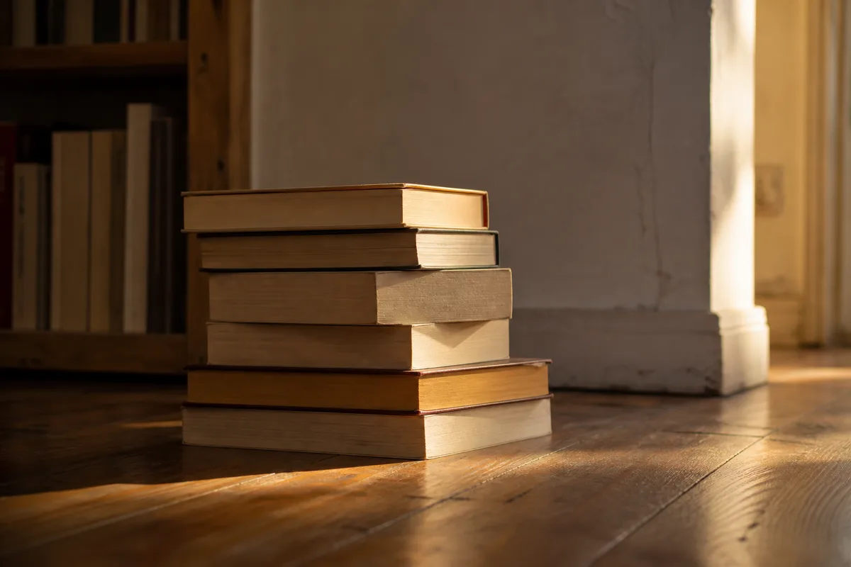 Pile de livres non lus posée au sol contre un mur, dans la lumière du soir